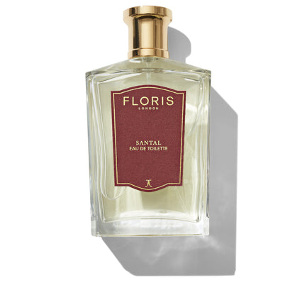 A clear glass bottle of Santal by Floris London Eau de Toilette, adorned with a gold cap and a red label, exuding the classic charm of a men's fragrance. Shadows are cast to the right side.