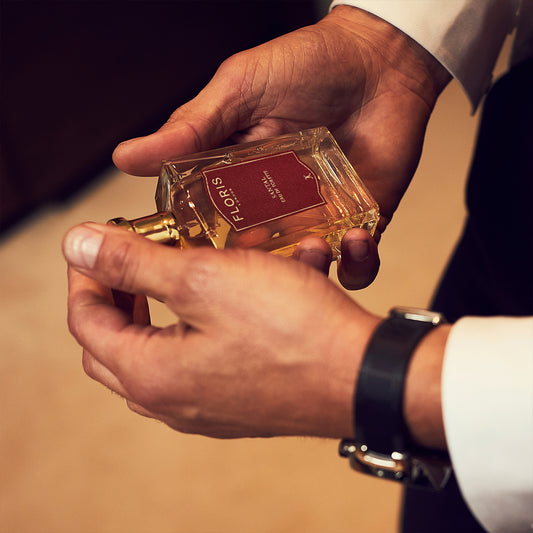 A person in a white shirt and black watch holds a Floris London "Santal" bottle, capturing a men’s signature scent with woody fougère notes.