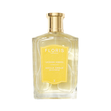 A clear glass bottle of Floris London EU Soulle Ámbar perfume with a gold cap, yellow label, and light yellow liquid inside.