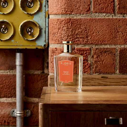 A bottle of Floris London Special No. 127 - Eau de Toilette, a citrus floral scent, sits on wood by a brick wall and vintage yellow electrical panel.