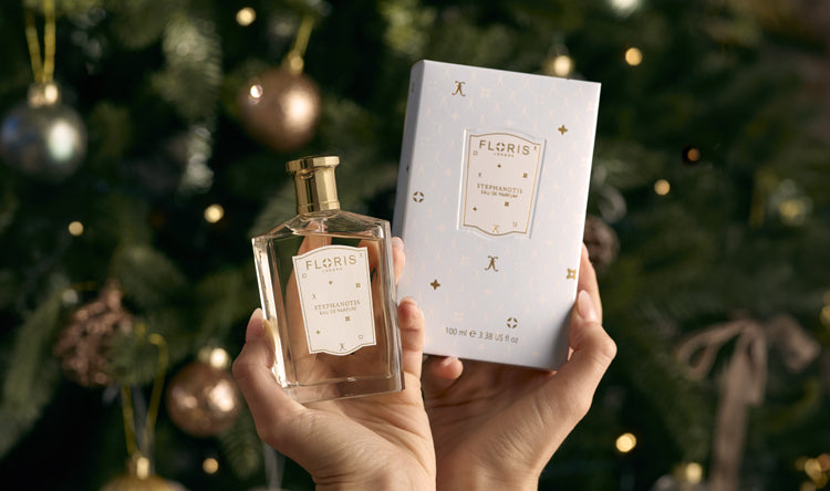 A Limited Edition Stephanotis fragrance from Floris London, in front of a Christmas tree adorned with ornaments and lights. This luxurious gift is perfect for the holiday season.