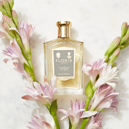 A bottle of Floris London Tuberose in Silk - Eau de Parfum sits on marble, surrounded by pink and white tuberose flowers for a delicate floral scent.