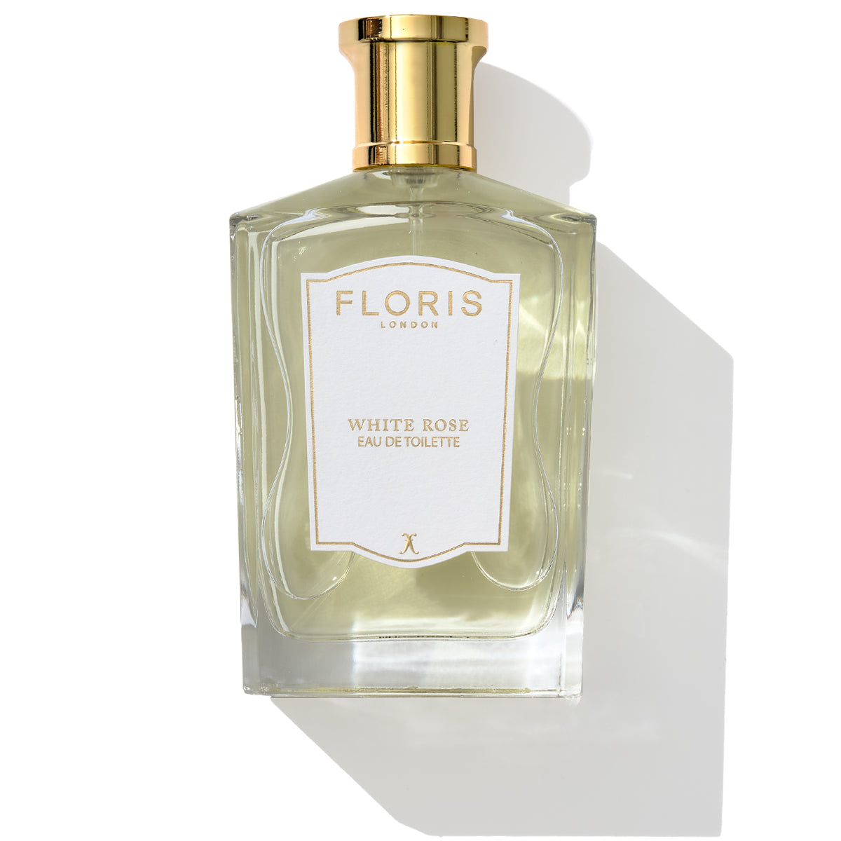 A rectangular glass bottle of Floris London's White Rose Eau de Toilette with a gold cap, exudes the essence of velvet roses and warm amber. The bottle casts a shadow to the right.