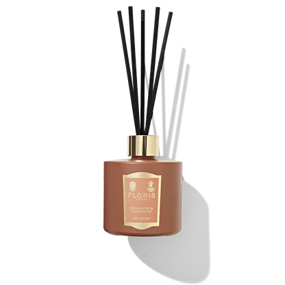 Burnt orange reed diffuser with 5 black reeds placed in the top. an Orange and gold label reads ' Floris London cinnamon and tangerine reed diffuser'.