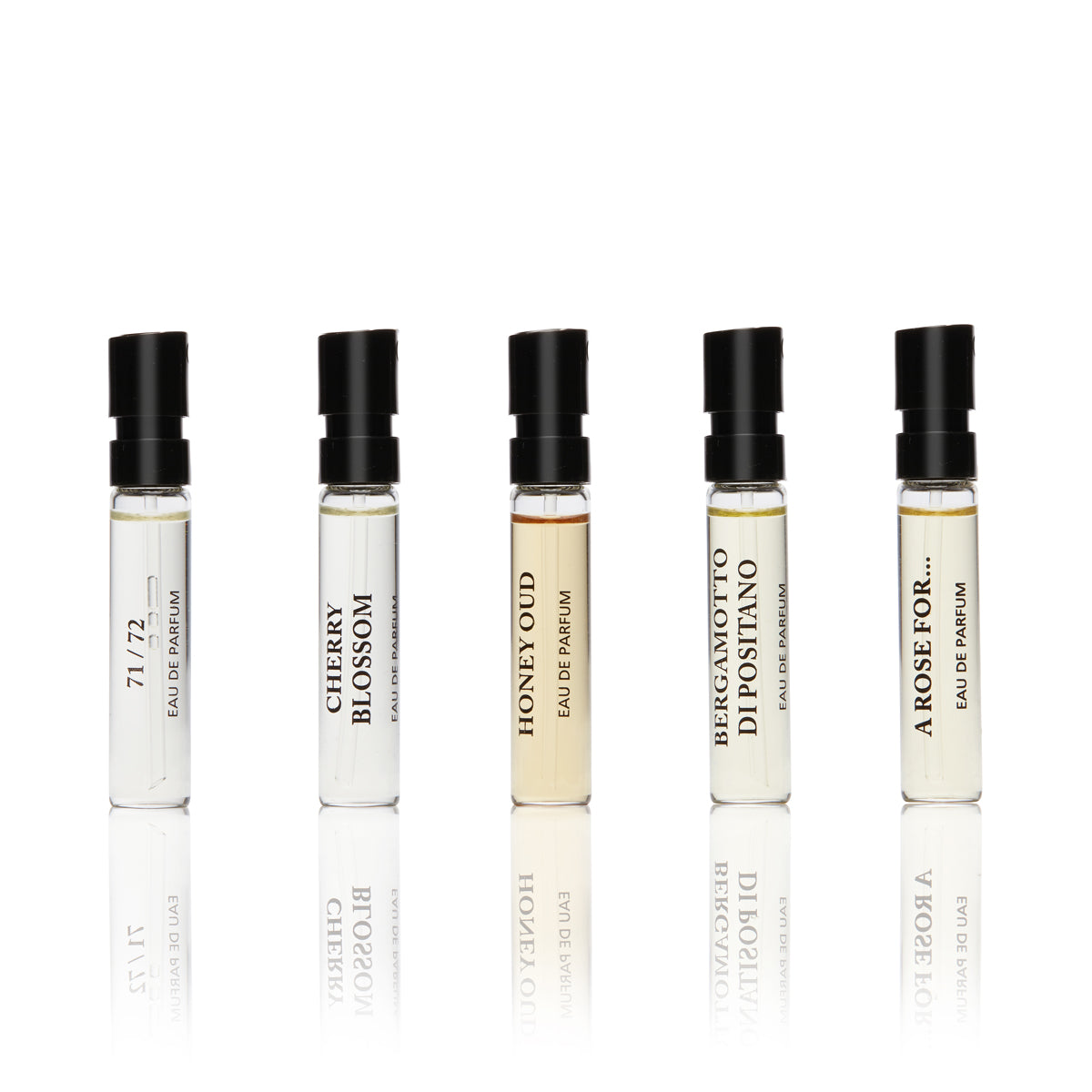 Five small clear glass vials with black writing on each, and black spray nozzles. containing the Private Discovery Collection