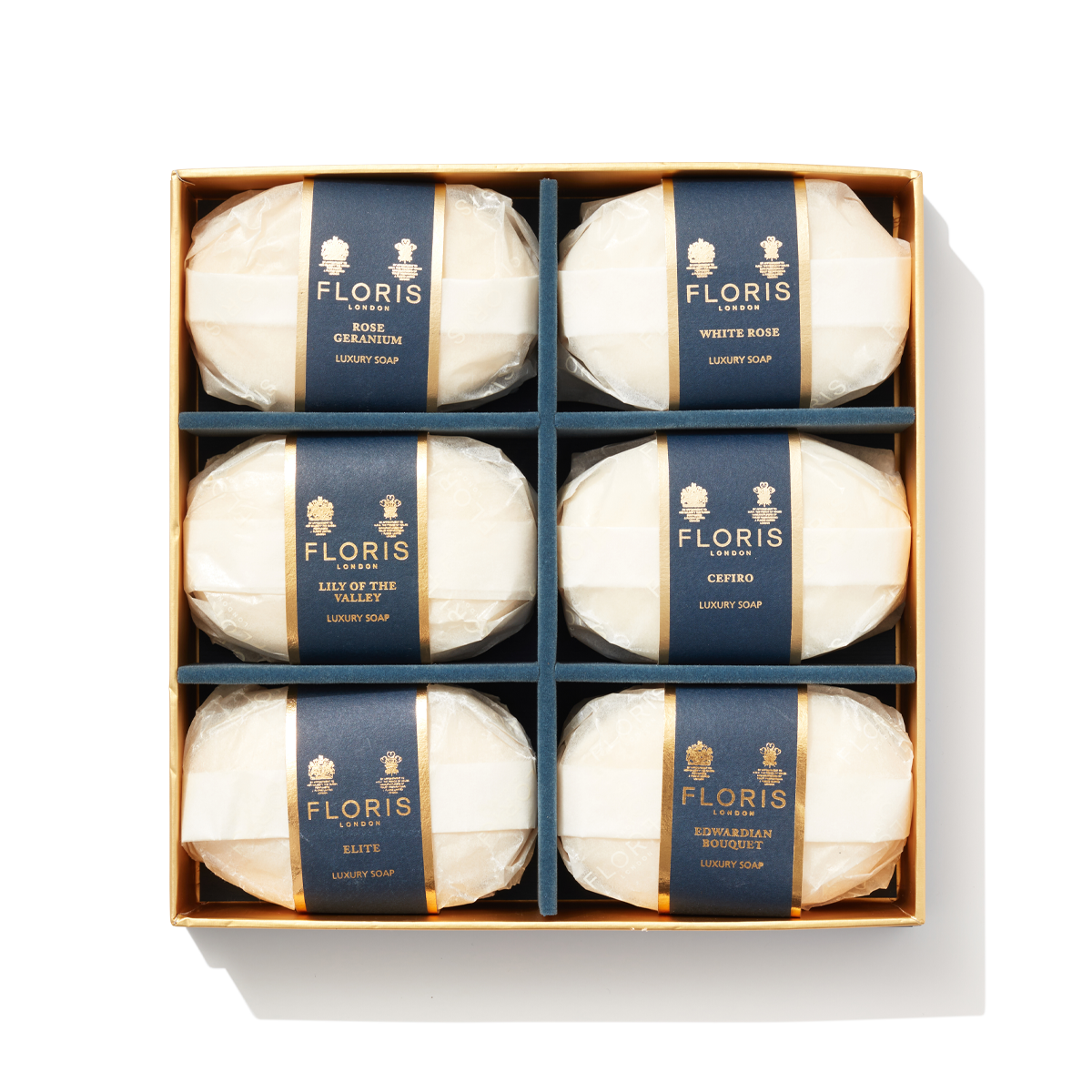6 bars of white oval shaped soap wrapped in paper with navy and gold labels in a large box. Containing Luxury Soap Collection