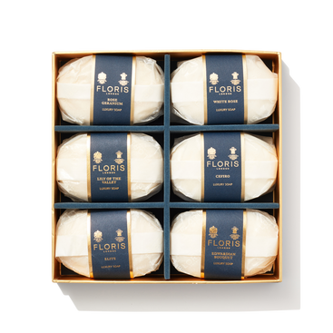 6 bars of white oval shaped soap wrapped in paper with navy and gold labels in a large box. Containing Luxury Soap Collection