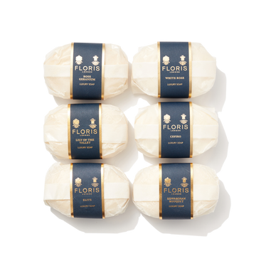 6 bars of white oval shaped soap wrapped in paper with navy and gold labels. Containing Luxury Soap Collection 