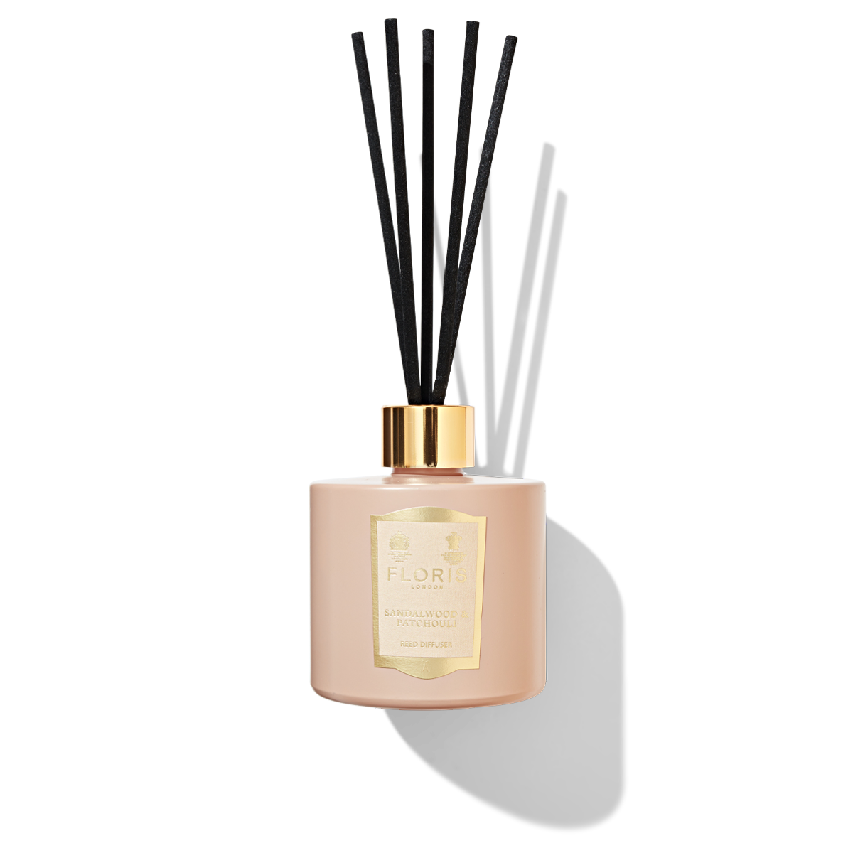 A light pink reed diffuser bottle with 5 black reeds in the top. a light pink and gold label attached with Sandalwood and patchouli printed on it.